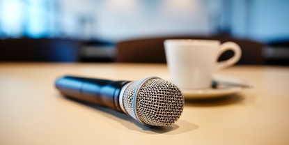 Cenário para a conferência com a imprensa: microfone e xícara de café em uma mesa.